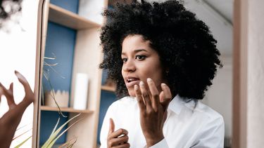 Vrouw kijkt in spiegel naar acne-littekens