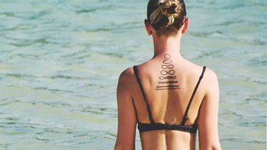 meisje met tattoos die op het strand zit, tattoo cliché